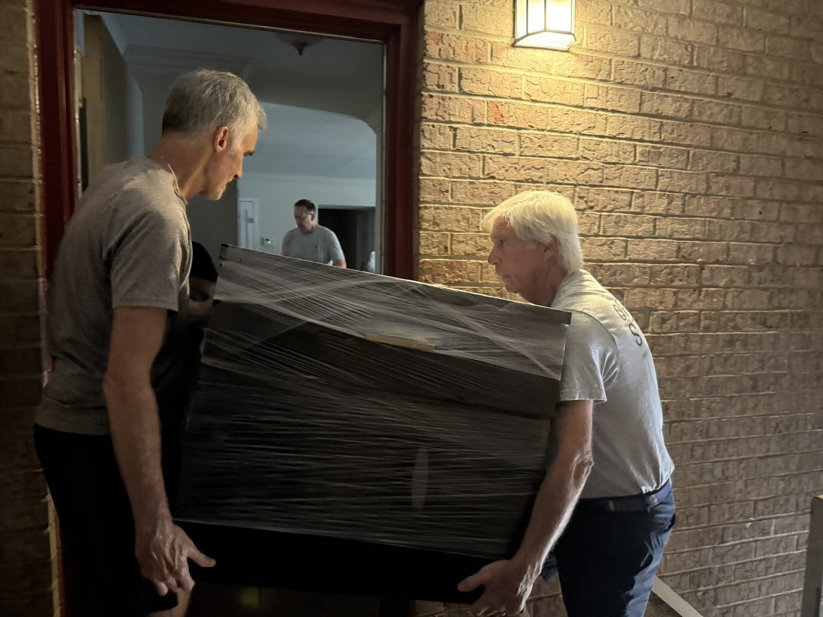 Two OTS Rockville volunteers carrying a wrapped mattress at a delivery