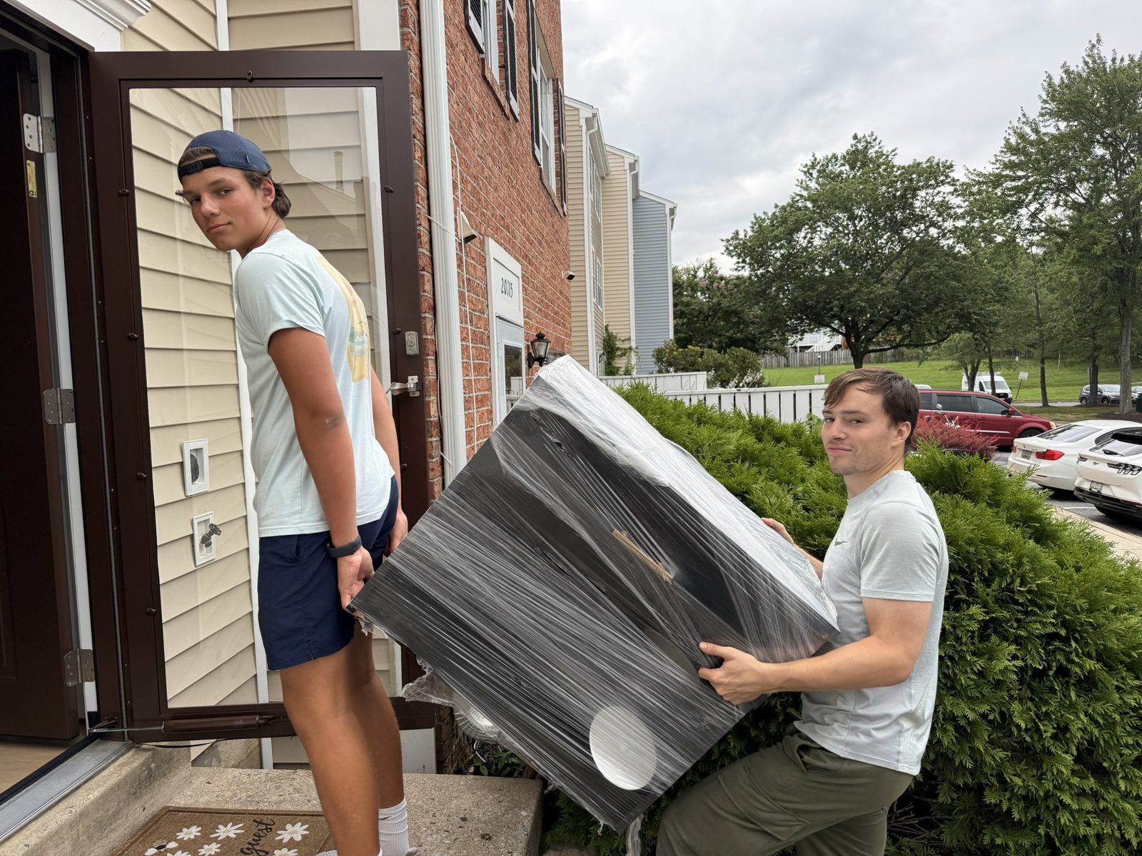 Two young volunteers from the St. Pat's Youth Group carrying a wrapped TV into a townhouse